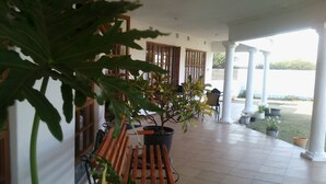 A covered outdoor area with a wooden bench, potted plants, and a view of a body of water. - Moko Motel (Mahalapye)