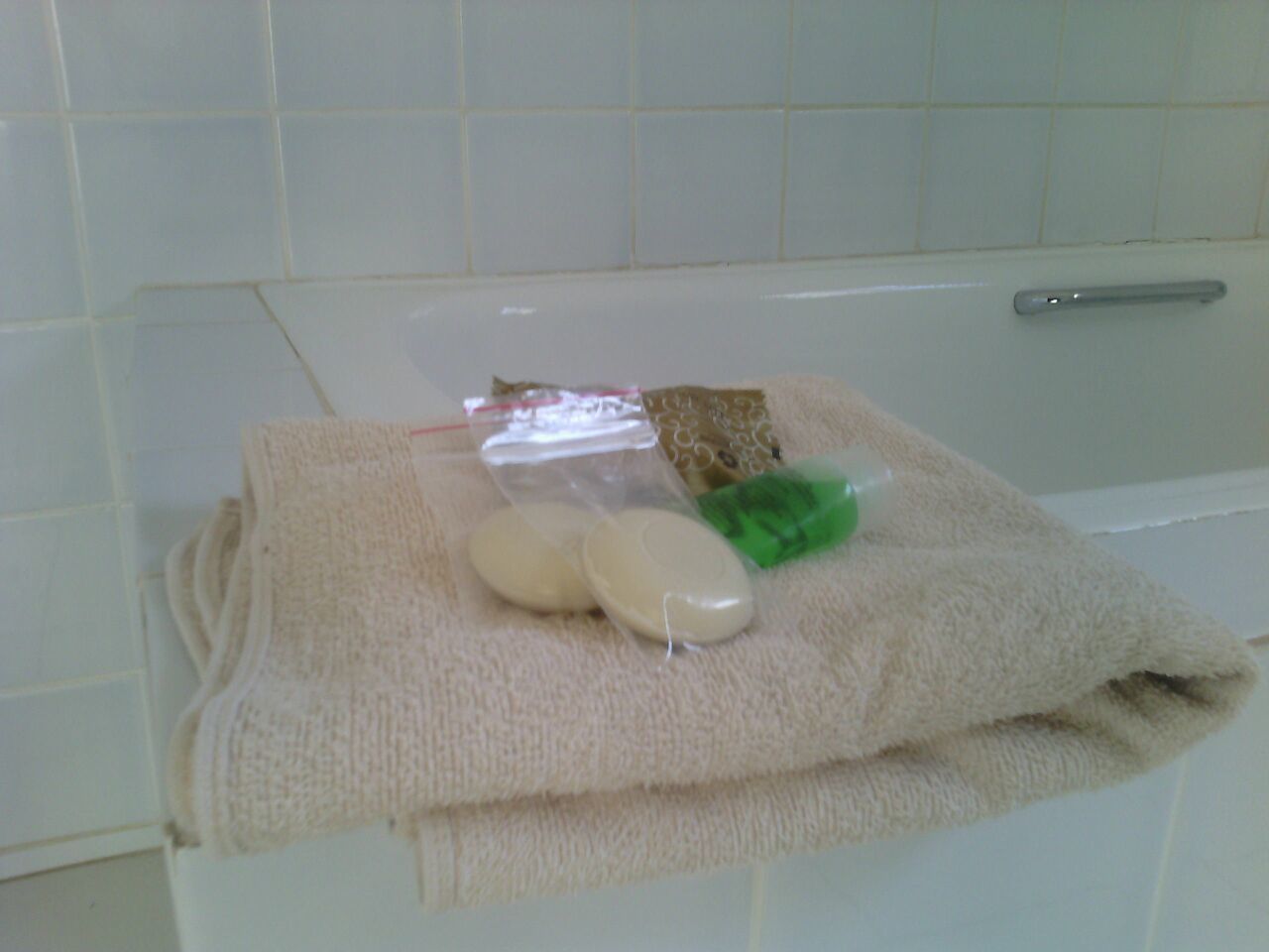 Un baño con una bañera blanca, una toalla, un jabón y una pequeña bolsa de plástico.