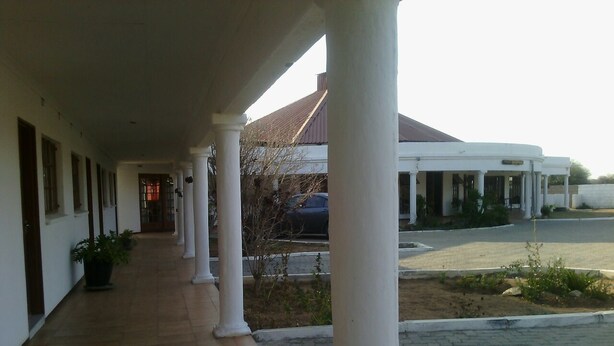 A covered walkway with columns, leading to a building with a tiled roof. - Moko Motel (Mahalapye)