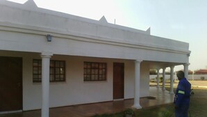 A building with a covered patio area, columns, and a person standing with a hose. - Moko Motel (Mahalapye)