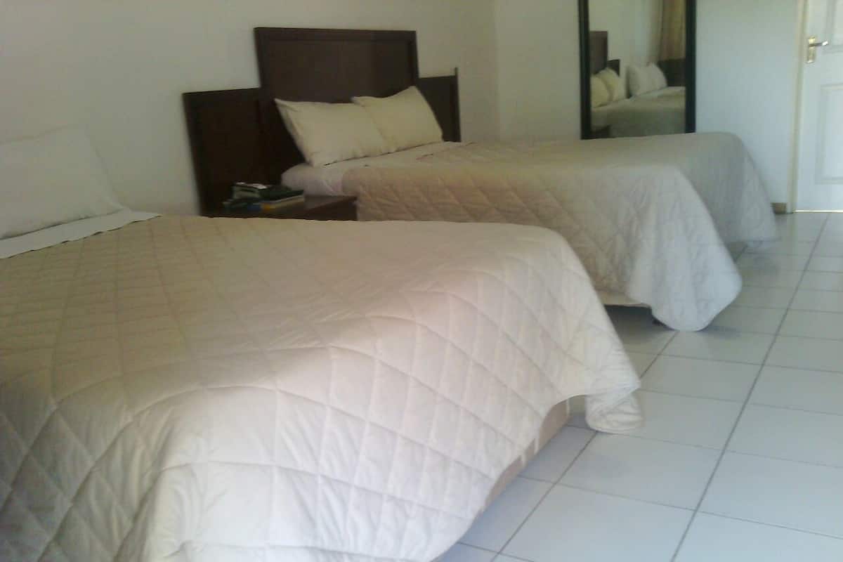 A hotel room with two beds, each with a quilted bedspread and a nightstand with a lamp.