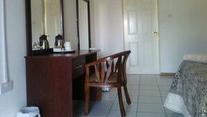 A hotel room with a wooden desk, a chair, a bed with a patterned bedspread, a white door, and an air conditioning unit on the wall. - Moko Motel (Mahalapye)