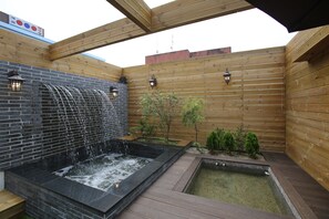 A wooden deck with a hot tub and a small pond, surrounded by wooden walls and a brick wall with a waterfall feature. - Hotel Cello Guri (Guri)