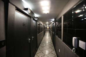 Un pasillo largo y estrecho con puertas de madera oscura, cada una con un número. El suelo tiene un diseño de baldosas con motivos.