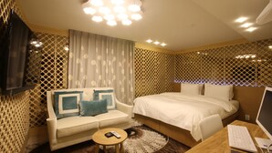 Habitación de hotel con cama, sofá, escritorio con computadora, televisor y pared con diseño.