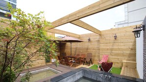 Una terraza de madera con un jacuzzi, una mesa de comedor con sillas y un pequeño jardín.