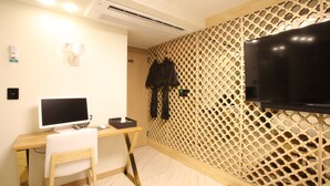 Una habitación con un escritorio de madera, una computadora, una silla, un televisor montado en una pared con diseño de celosía y un estante con objetos.