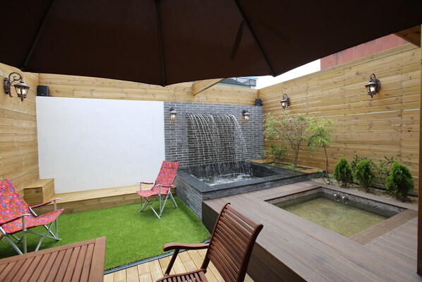 A wooden deck with a hot tub, two lounge chairs, and a small waterfall feature. - Hotel Cello Guri (Guri)
