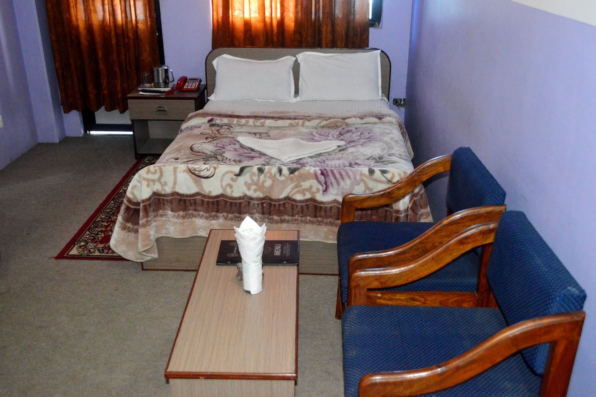 Una habitación de hotel con una cama, una mesita de noche de madera, un sofá azul y una pequeña mesa con una caja de pañuelos.