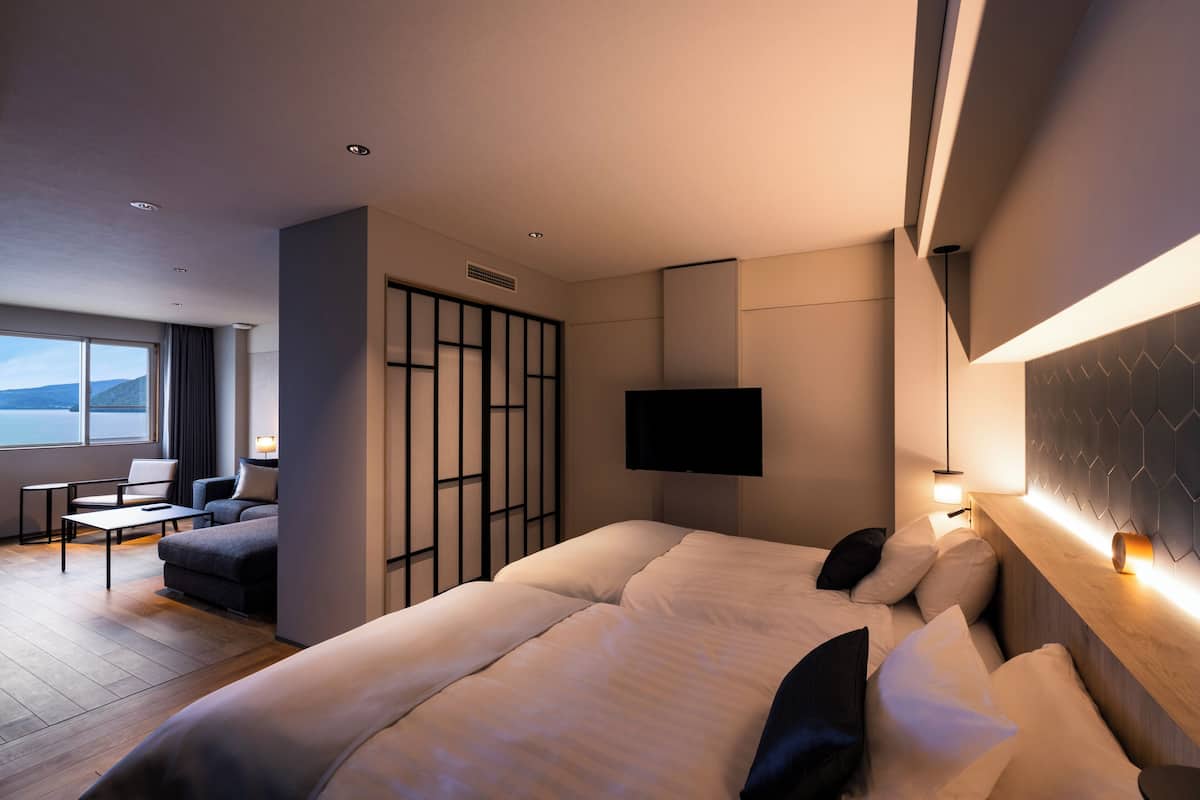 Une chambre d’hôtel moderne dotée d’un grand lit, d’un coin salon avec un canapé et une table, d’un t éléviseur fixé au mur et offrant une vue sur l’extérieur par une fenêtre.