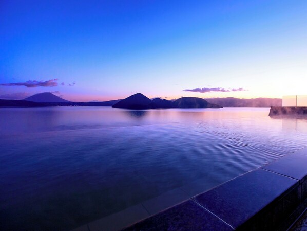 Uma área de piscina tranquila com vista para montanhas distantes e um pôr do sol.