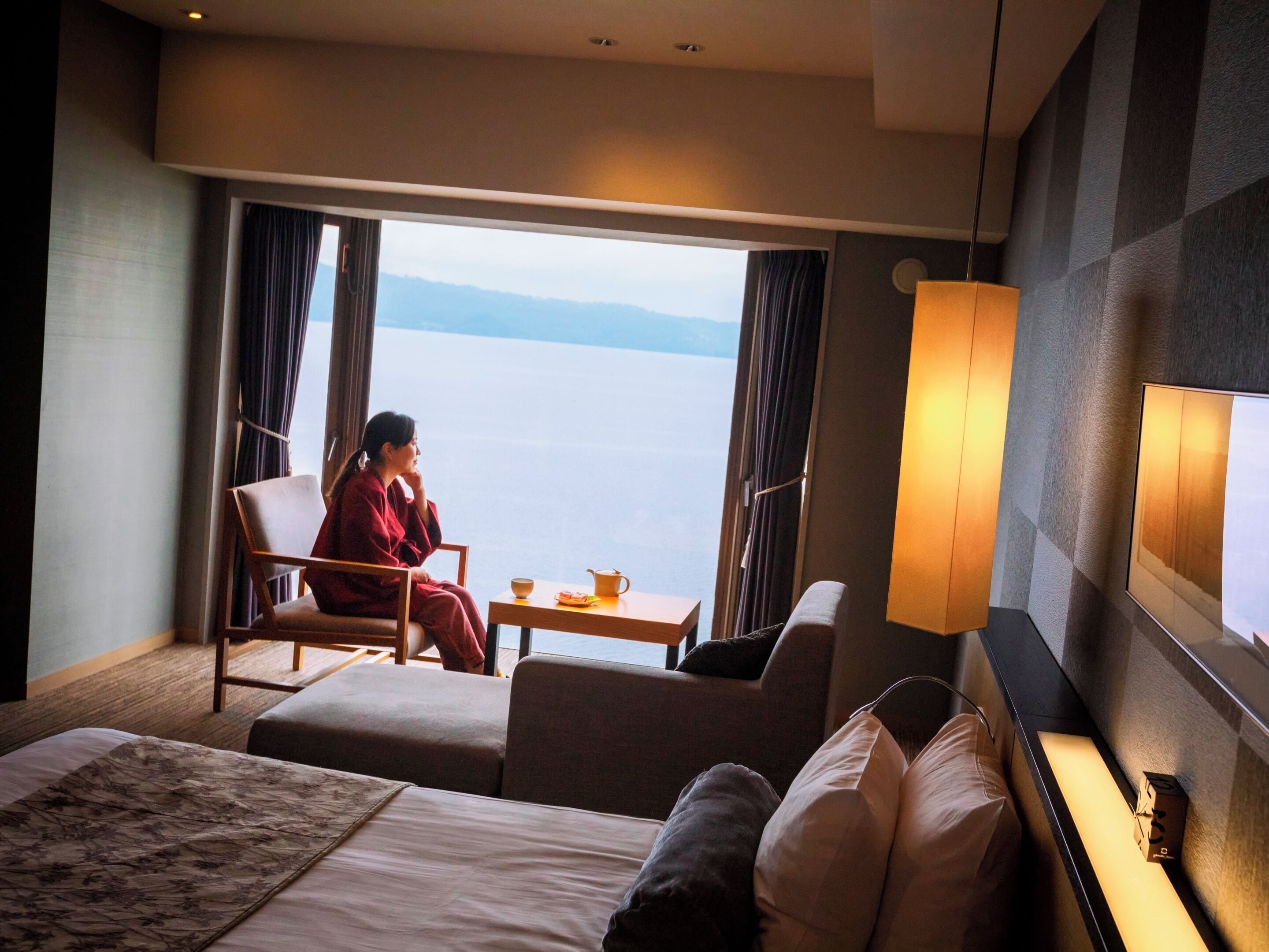 A hotel room with a bed, a sofa, a chair, a small table, and a view of the sea.