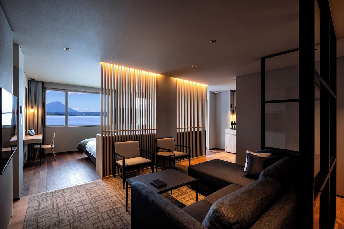 Une chambre d’hôtel moderne, dotée d’un canapé, de fauteuils, d’un bureau et offrant une vue sur la montagne grâce à de grandes fenêtres.