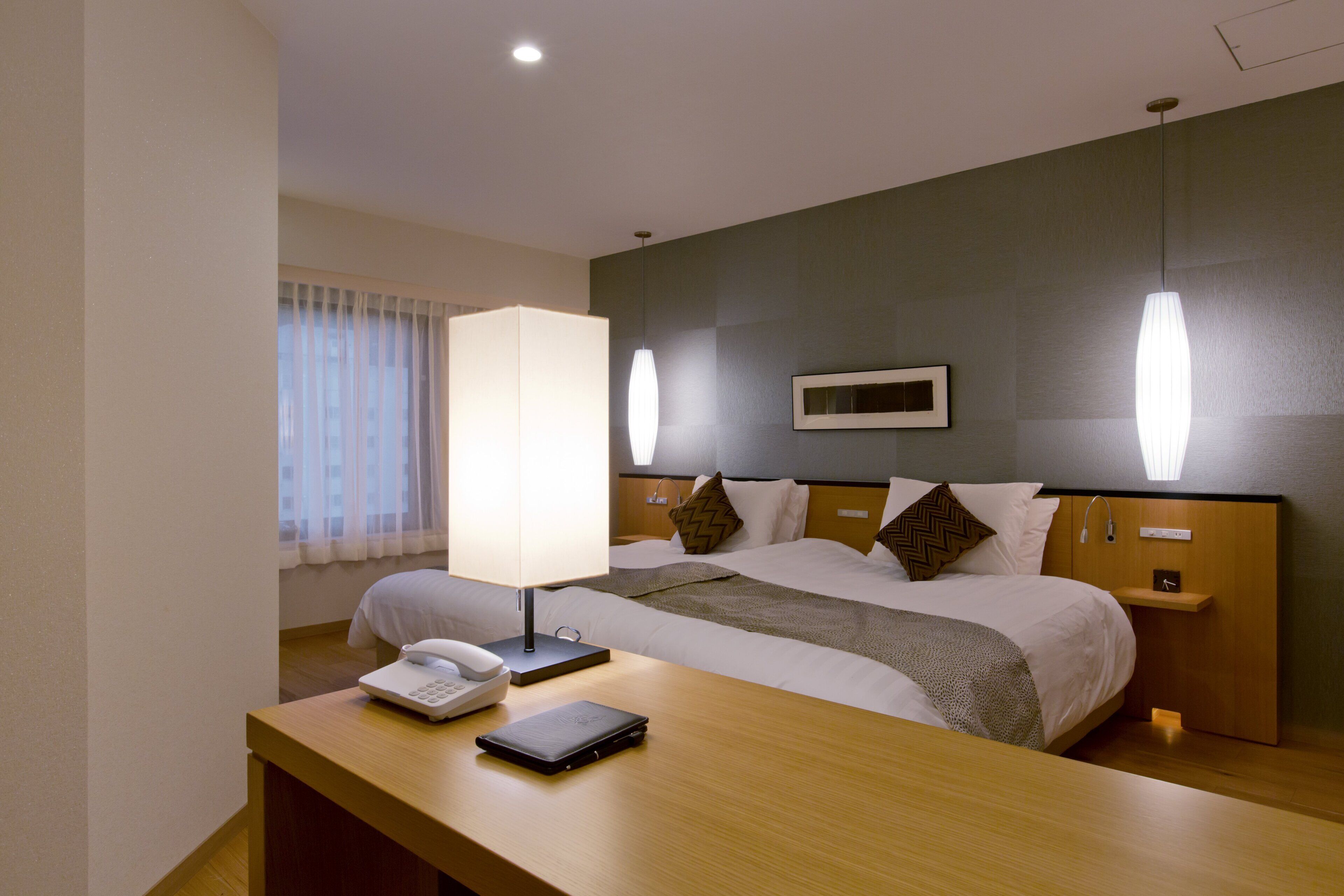 A hotel room with a bed, bedside tables, a lamp, a phone, and a small shelf.