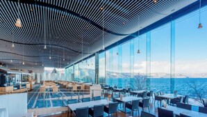 A modern restaurant with a view of the sea, featuring a high ceiling with a unique design, large windows, and a variety of seating arrangements. - The Lake View Toya Nonokaze Resort (Toyako)