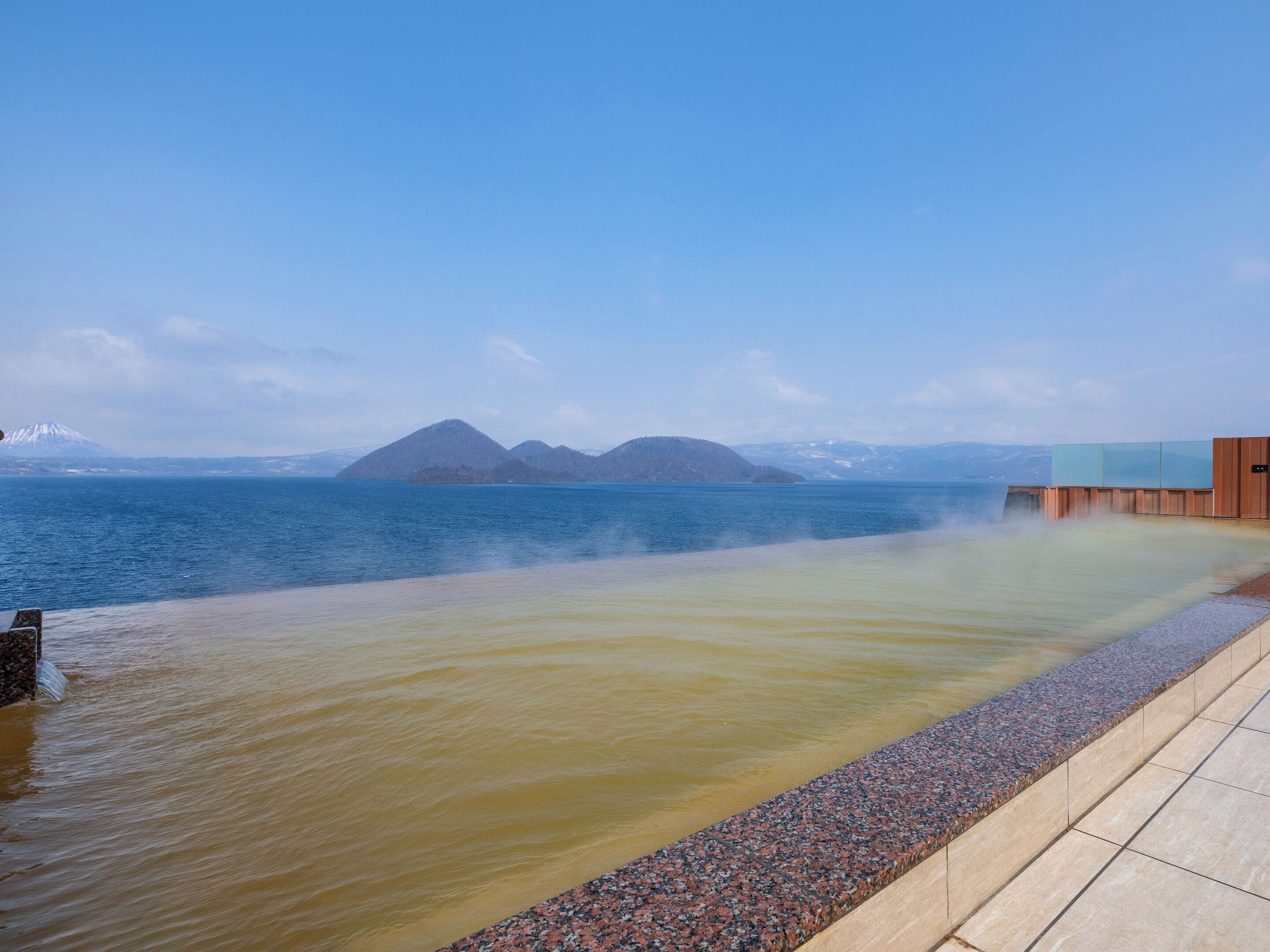 A spa area with a hot spring, a pebble-lined walkway, and a view of distant mountains.