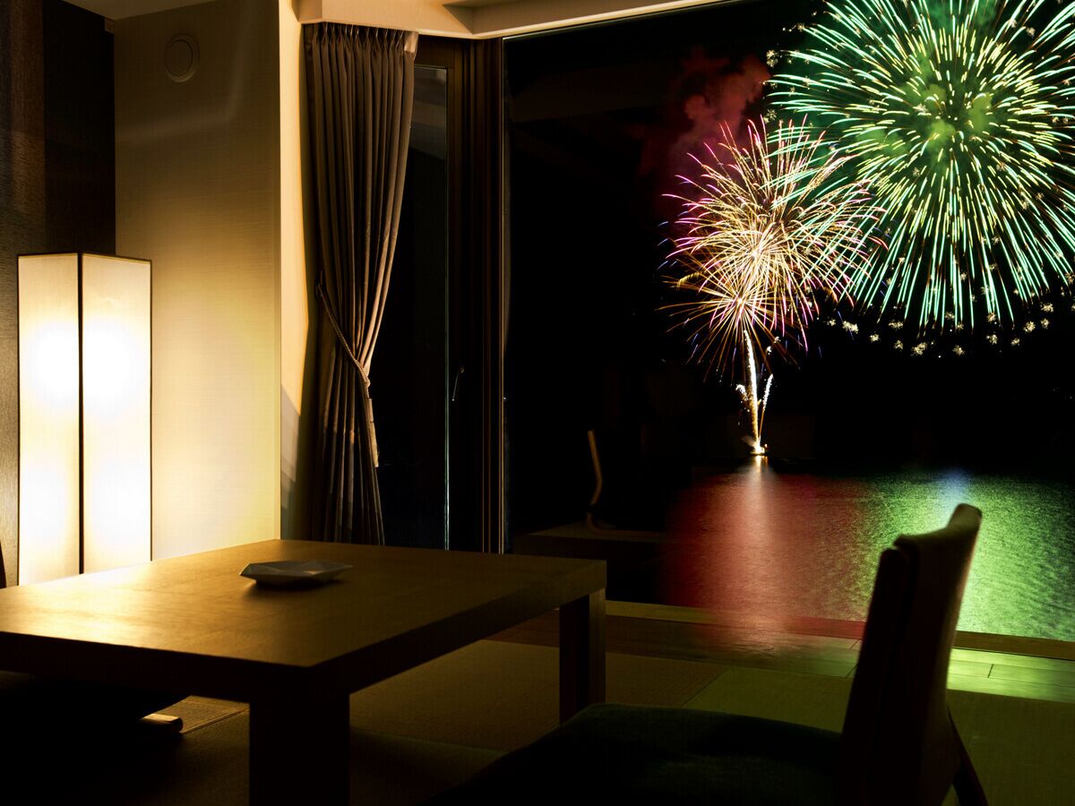 Habitación de hotel con una mesa, una silla, una lámpara y vistas a fuegos artificiales.