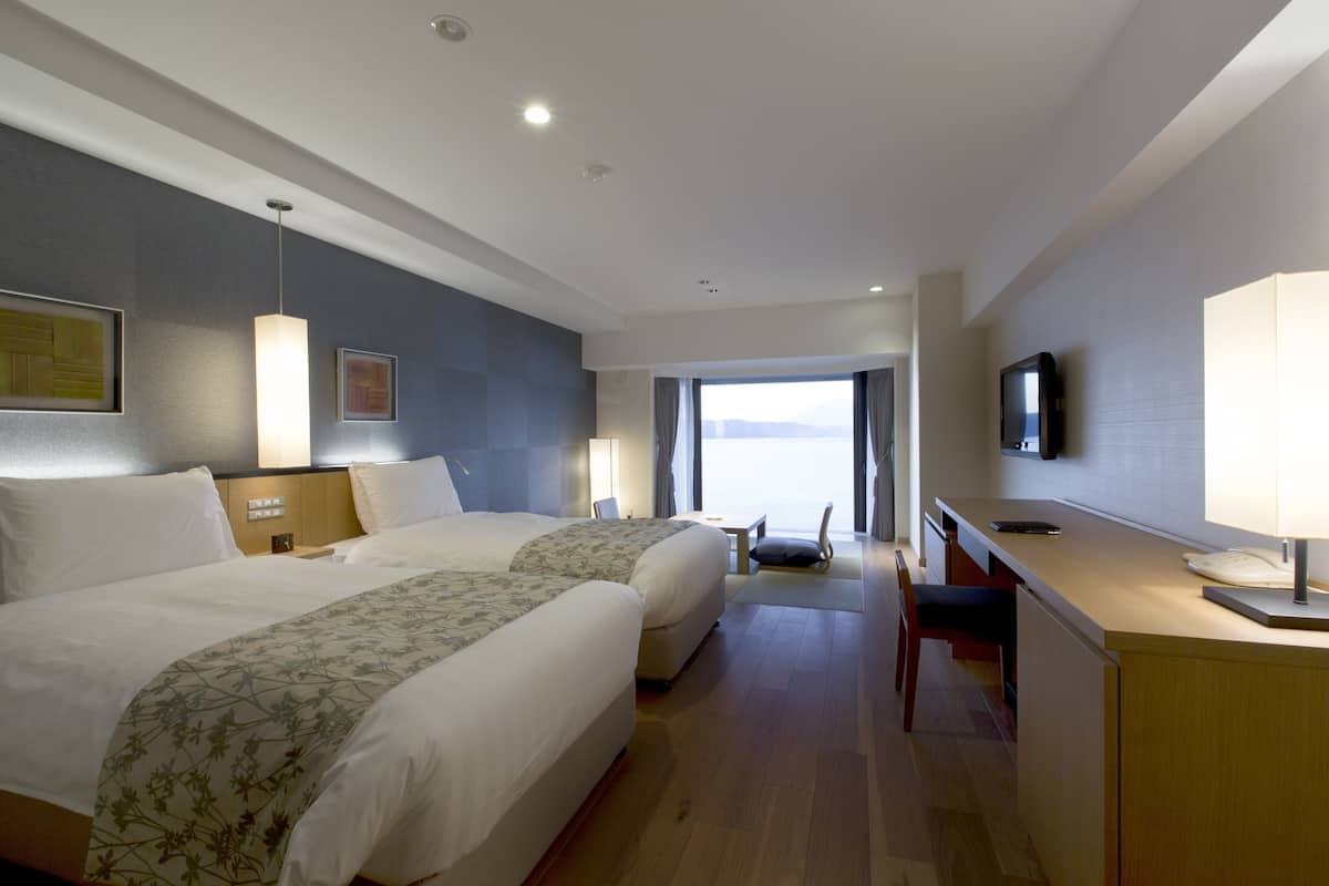Une chambre d’hôtel avec deux lits, un bureau, une chaise, une télévision et une fenêtre donnant sur un beau paysage.