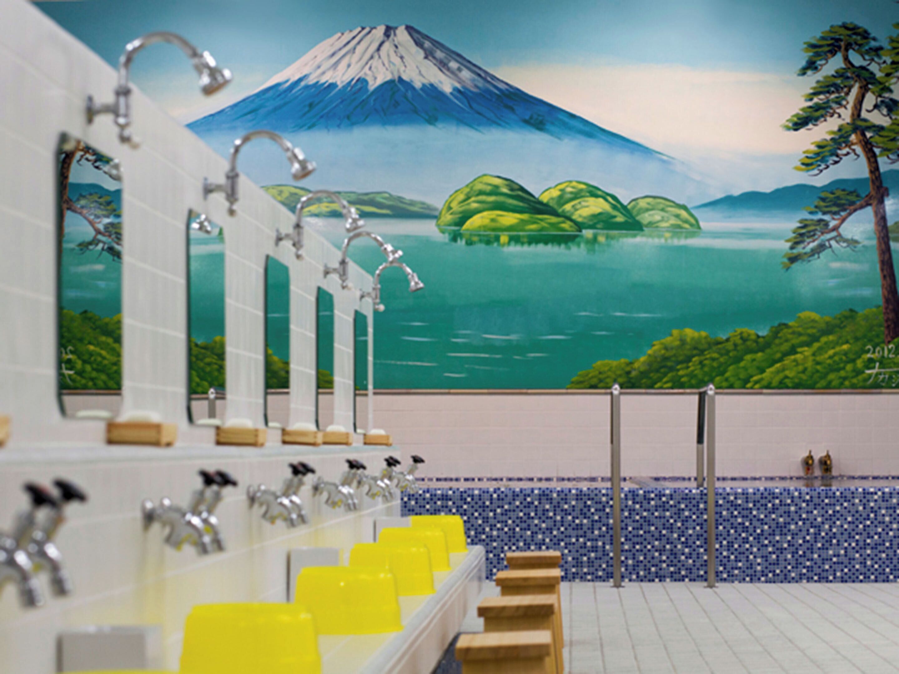 Ein Badezimmer mit mehreren Waschbecken, einer mit einer Berglandschaft bemalten Wand und einem blauen Fliesenboden.
