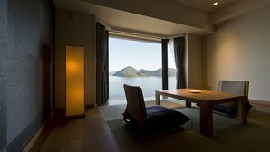 A room with a wooden table and chairs, a view of a body of water and mountains, and a large window with curtains. - The Lake View Toya Nonokaze Resort (Toyako)