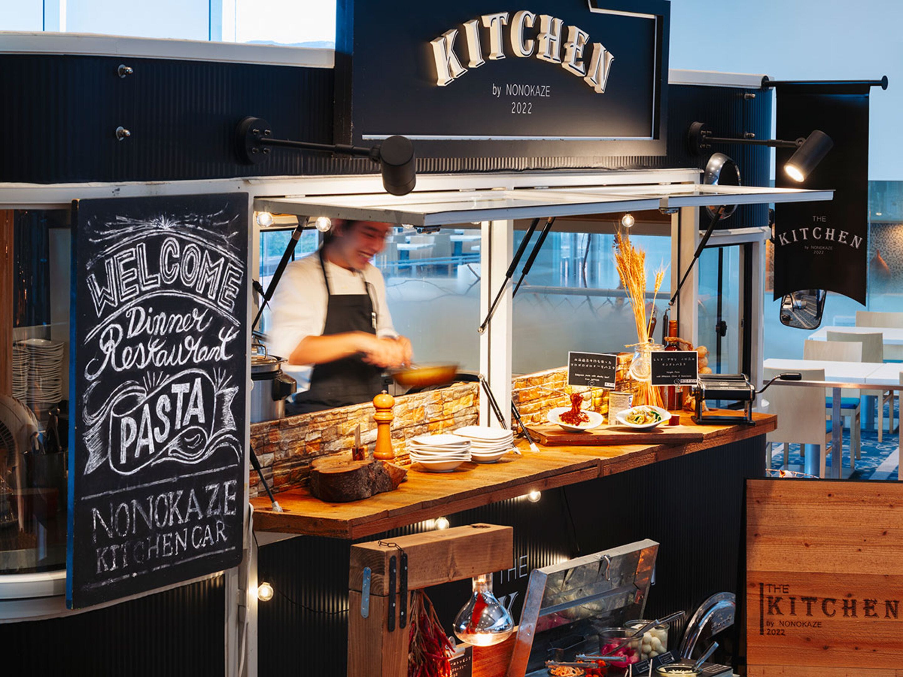 A food stall with a chalkboard sign reading 'Welcome Dinner Restaurant Pasta Nonokaze Kitchen 2022'.