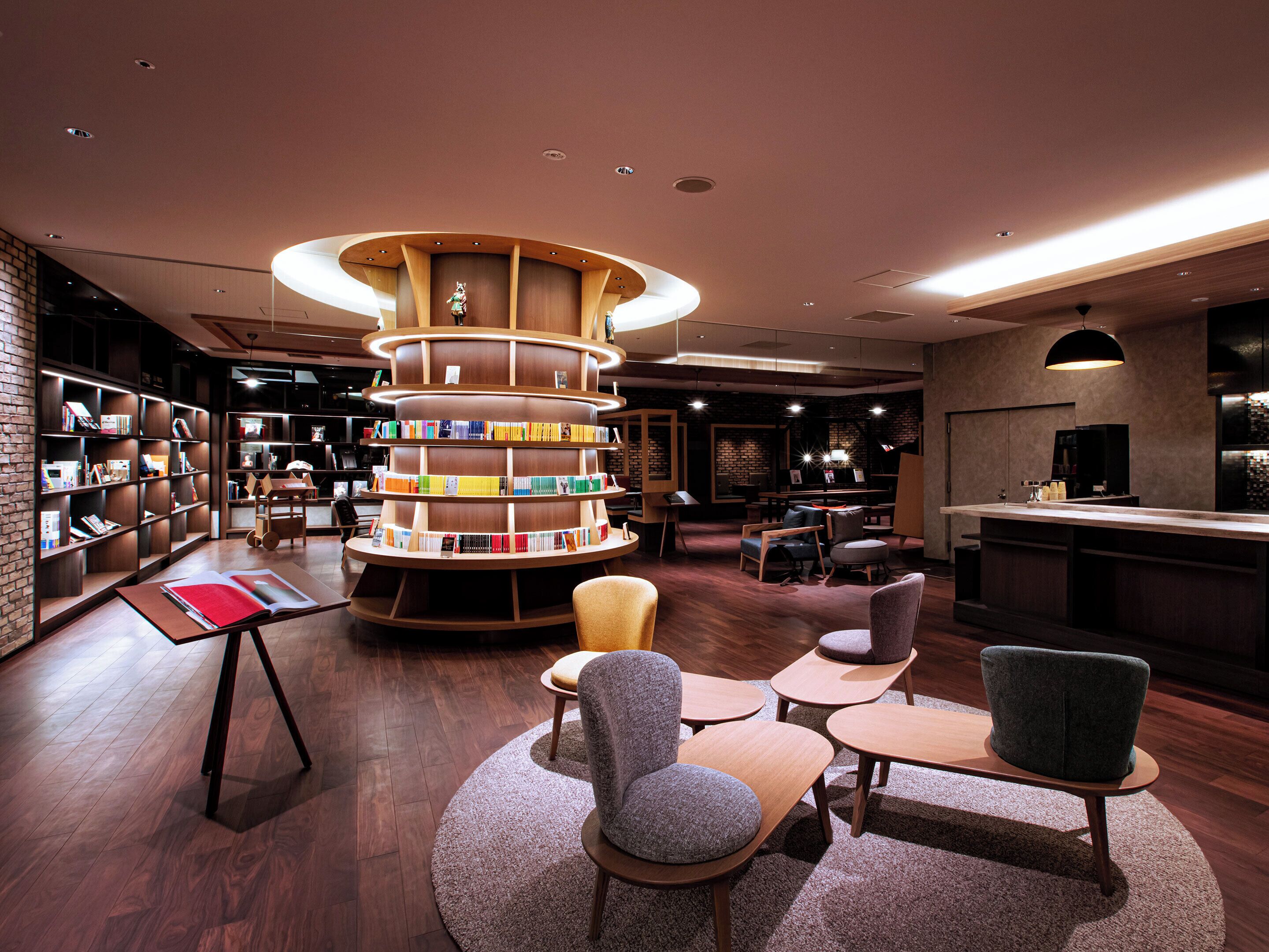 A modern library with a central circular bookshelf, multiple seating areas, and a bar counter.