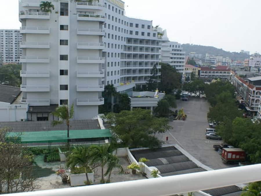 Hotel com vários andares, varandas, área de estacionamento e vista para a paisagem urbana circundante.