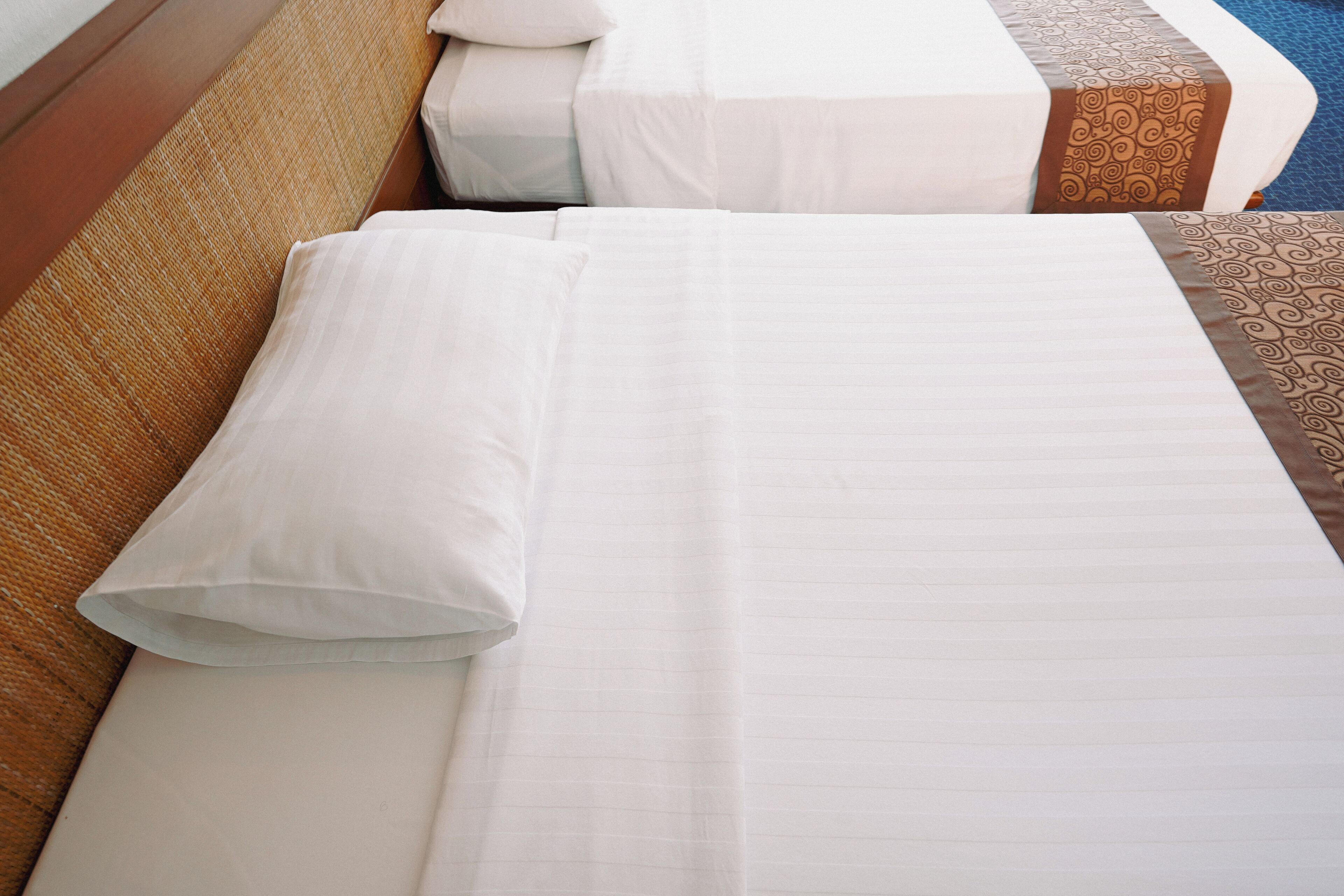 A neatly made bed with white linens and a pillow, a wooden headboard, and a patterned bed runner.