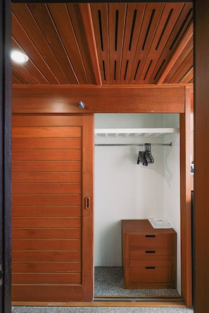 Une armoire en bois avec une porte coulissante, une petite table de chevet avec des tiroirs et un portant à vêtements.