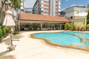 A swimming pool with a tiled deck, a pool bar, and a building with a tiled roof in the background. - Royal Twins Palace Hotel (Pattaya)
