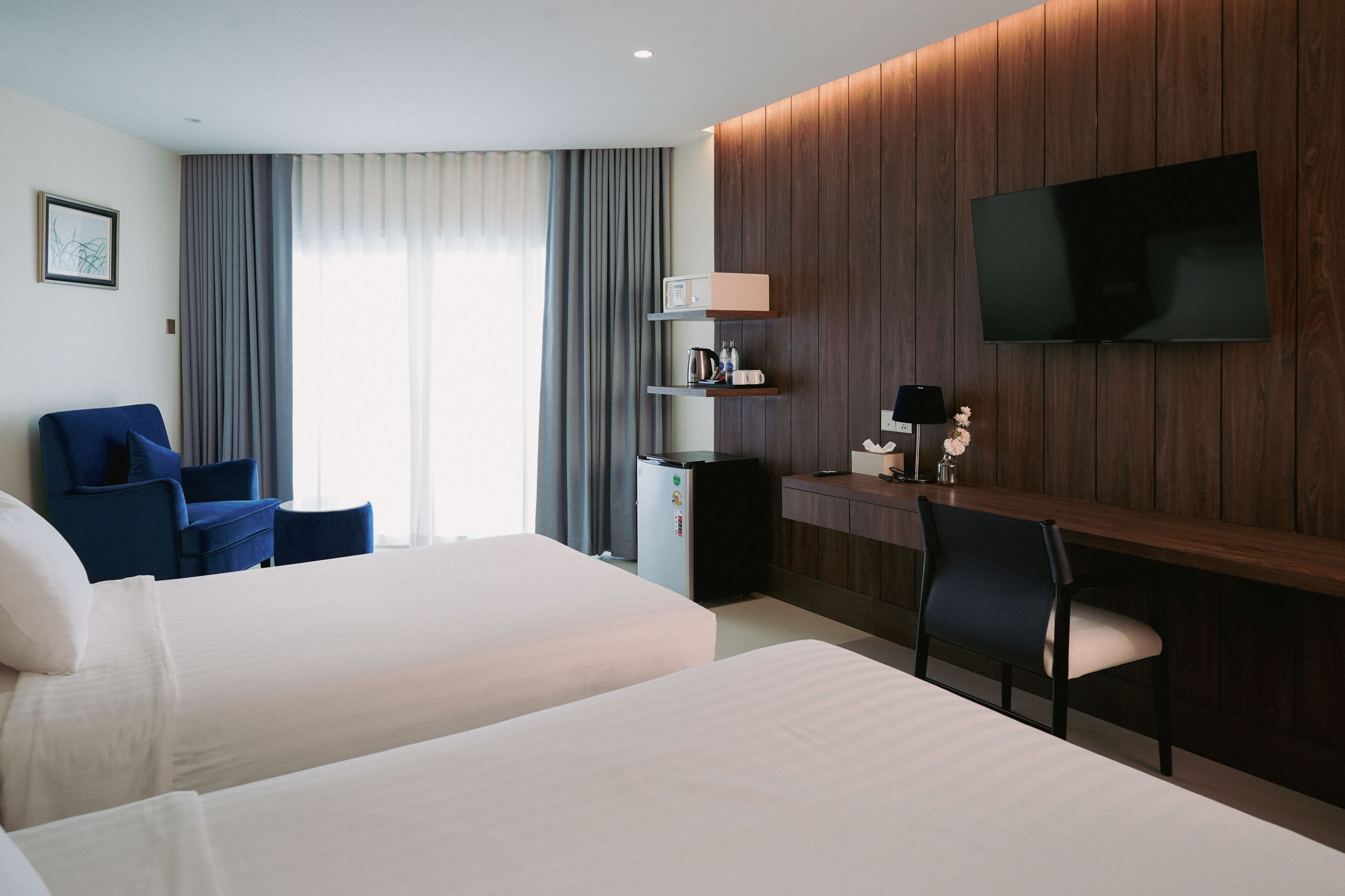 A hotel room with two beds, a desk, a chair, a TV, and a minibar.