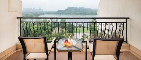 Un balcon avec deux chaises et une table, donnant sur une rivière et des collines.