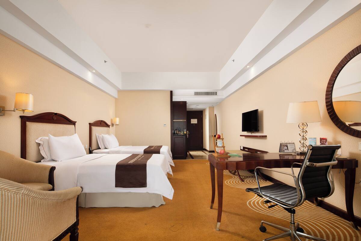 Une chambre d’hôtel avec deux lits, un bureau avec une chaise, une télévision et un miroir.
