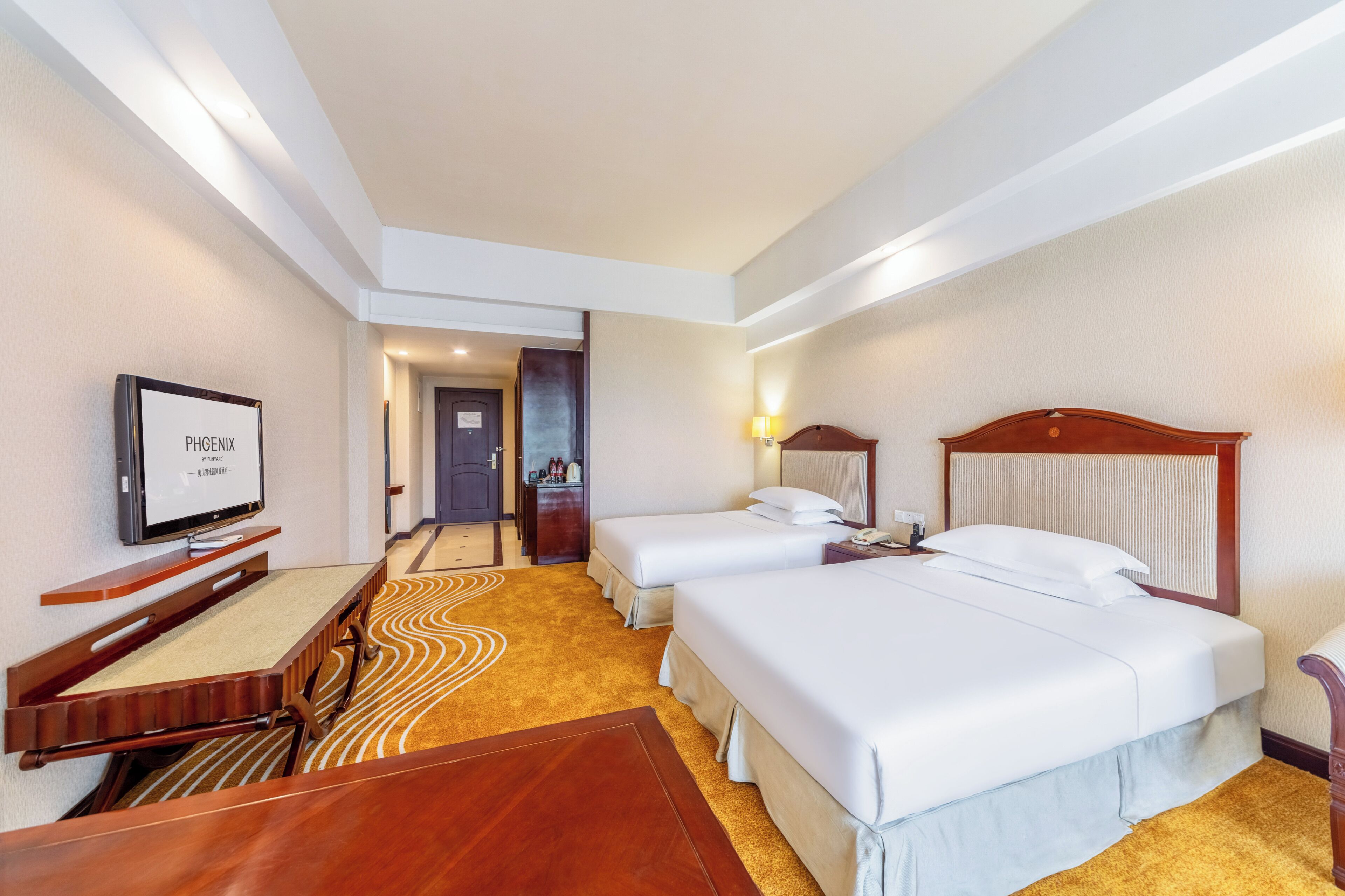 A hotel room with two beds, a TV, a desk, and a carpeted floor.
