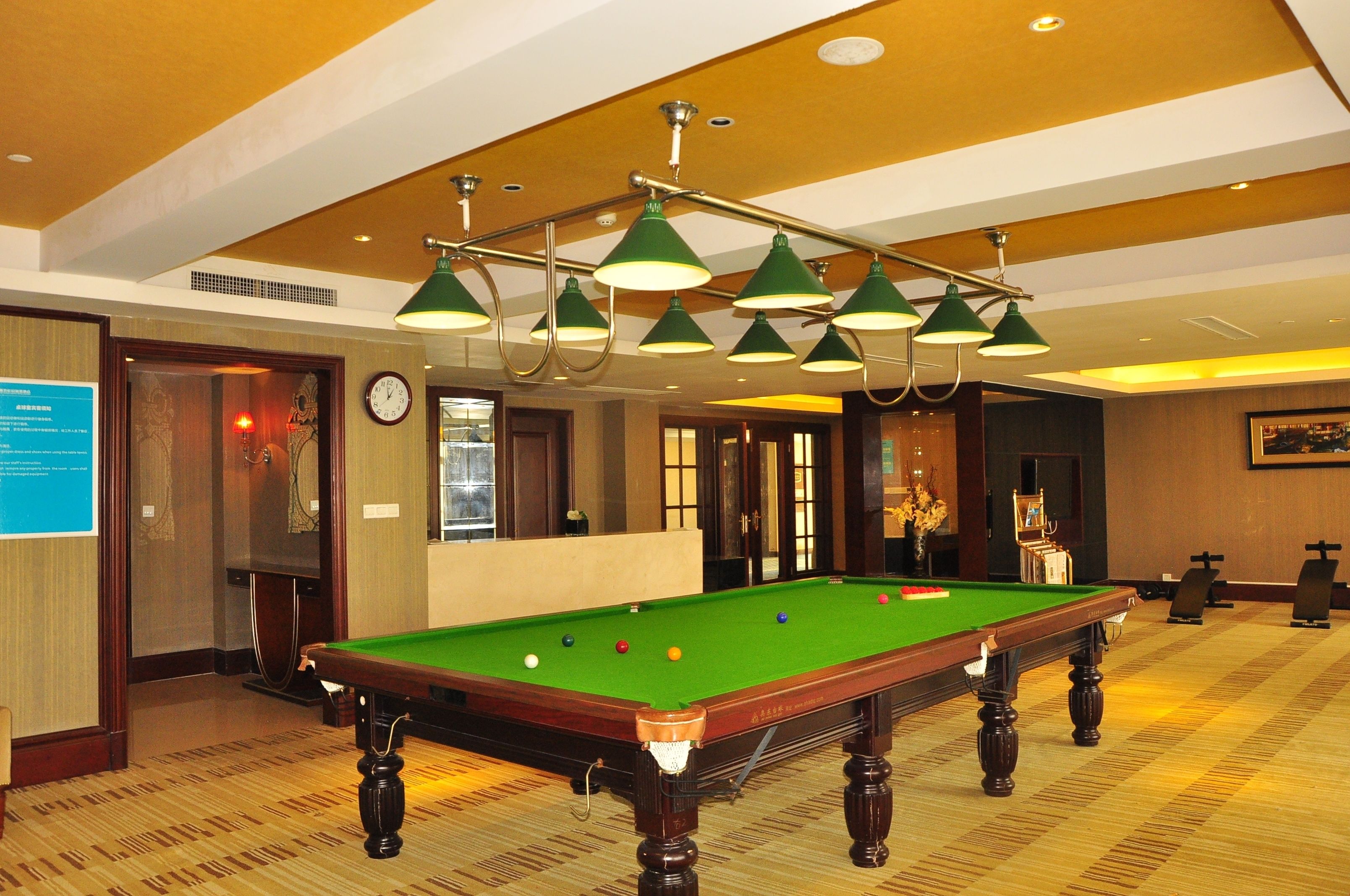 A pool table with a green felt surface, surrounded by a carpeted floor and wooden furniture.