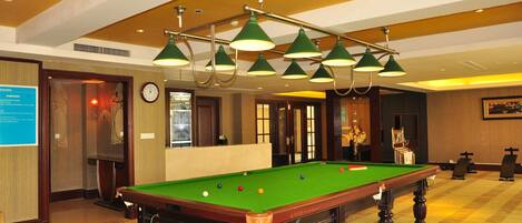 Une table de billard recouverte d’un drap vert, entourée d’un sol moquetté et de meubles en bois.