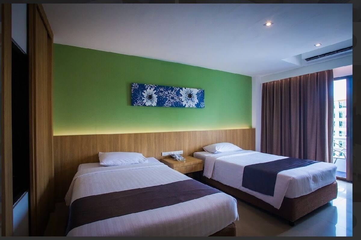Een hotelkamer met twee bedden, een groene accentmuur, een bloemkunstwerk en een raam met gordijnen.