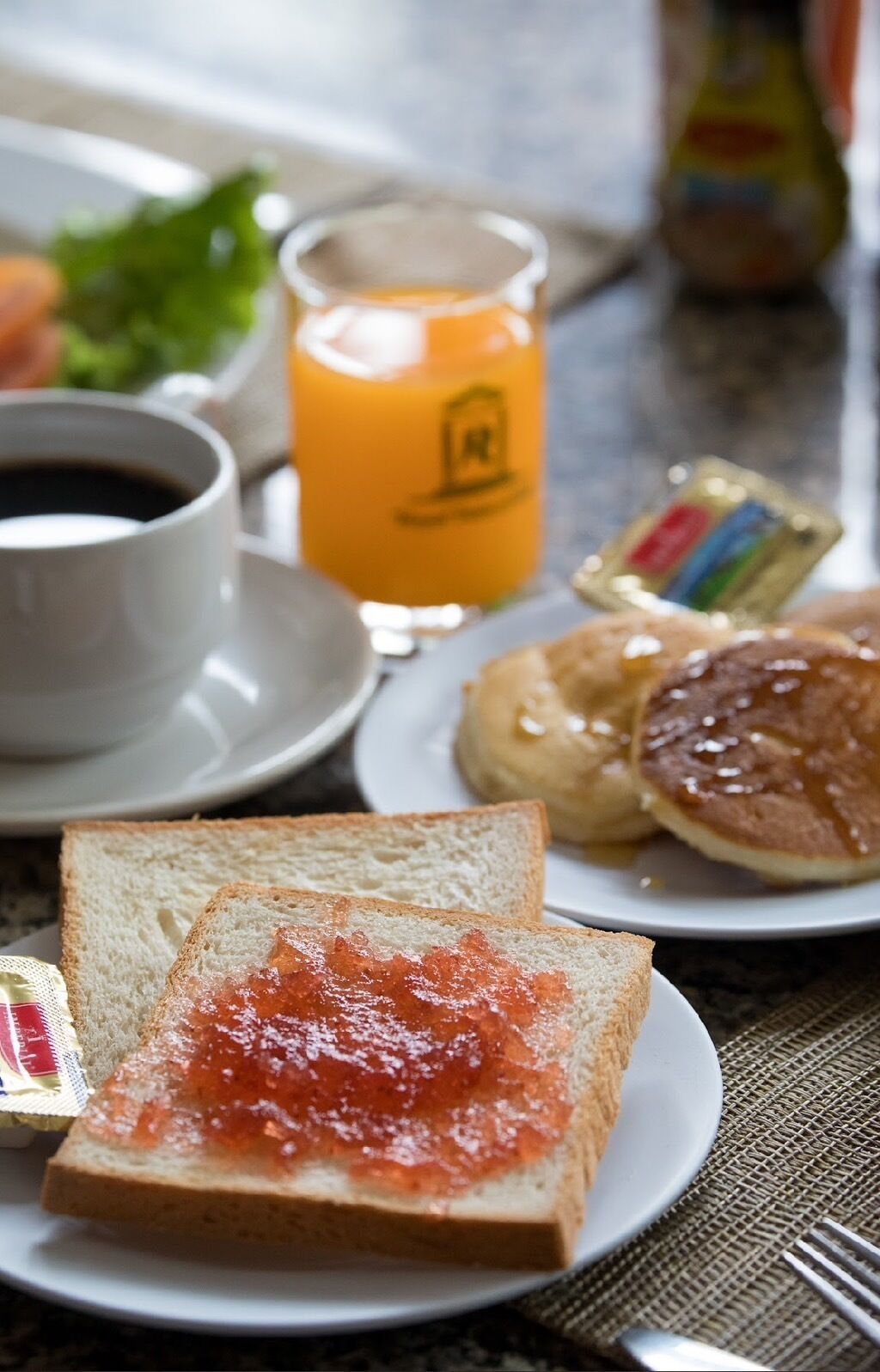 Ein Frühstückstisch mit Toast, Marmelade, Pfannkuchen, einer Tasse Kaffee und einem Glas Orangensaft.