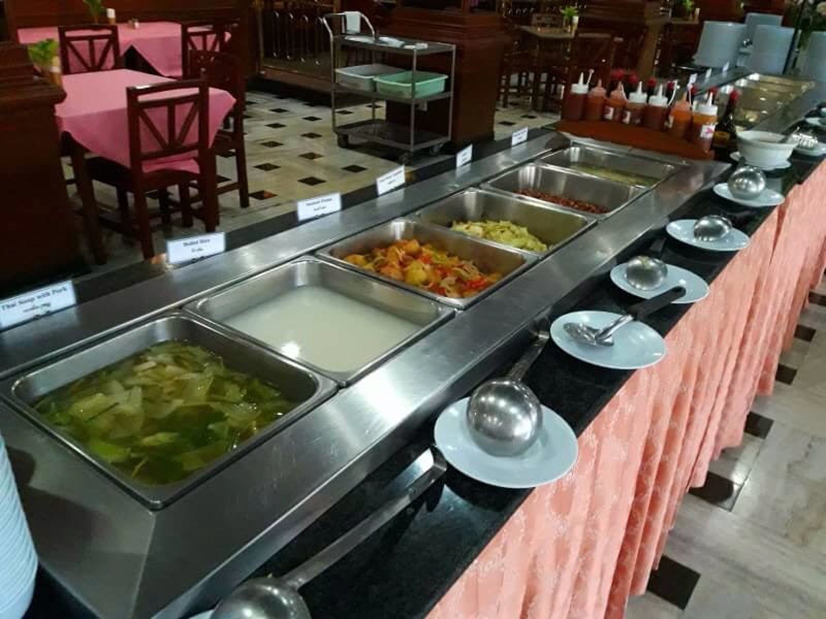 A buffet with various food options, including a green vegetable dish, a white creamy dish, and a red vegetable dish.