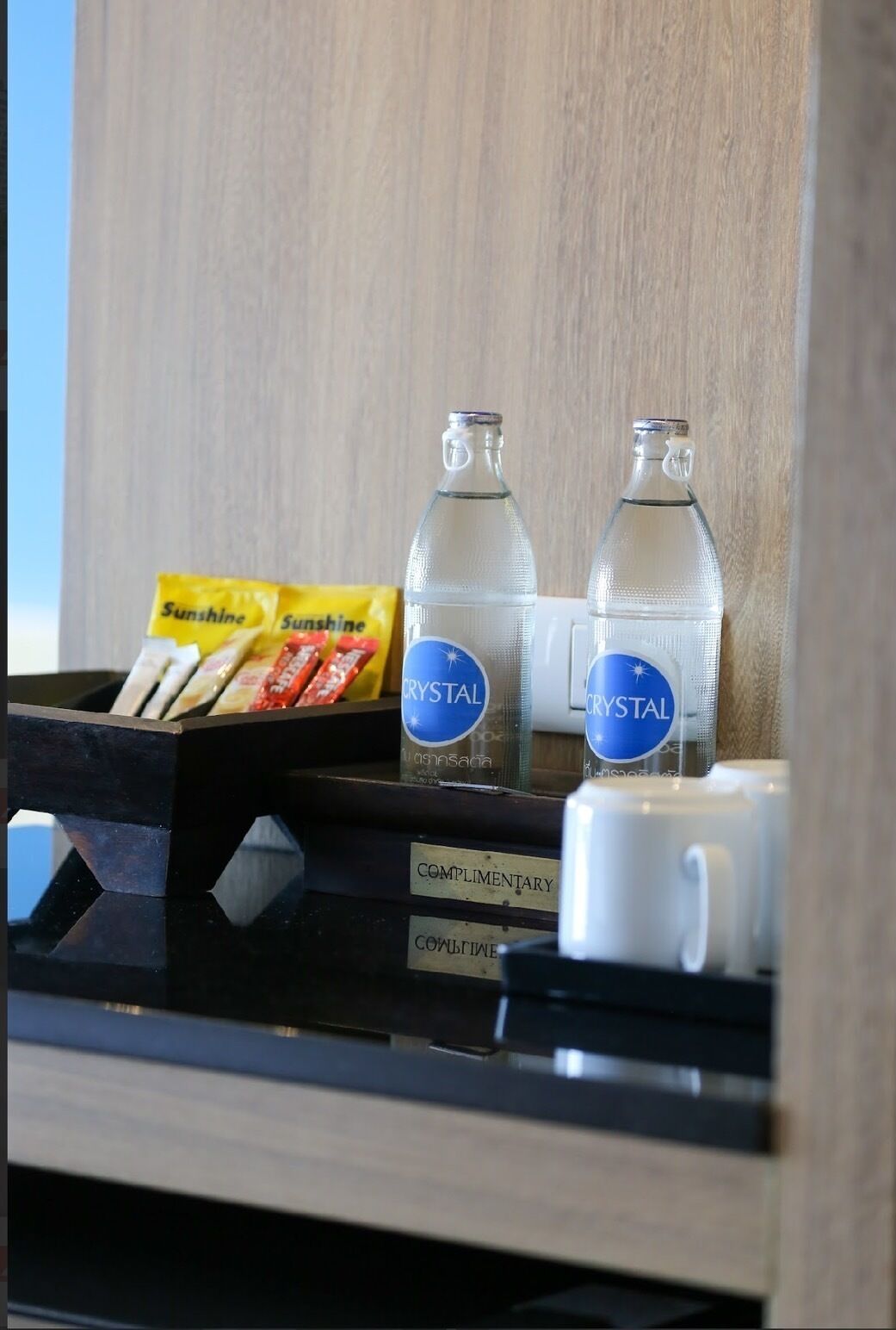 Een minibar met twee flessen Crystal water, een pakje Sunshine snacks en een witte beker met de tekst 'Complimentary'.
