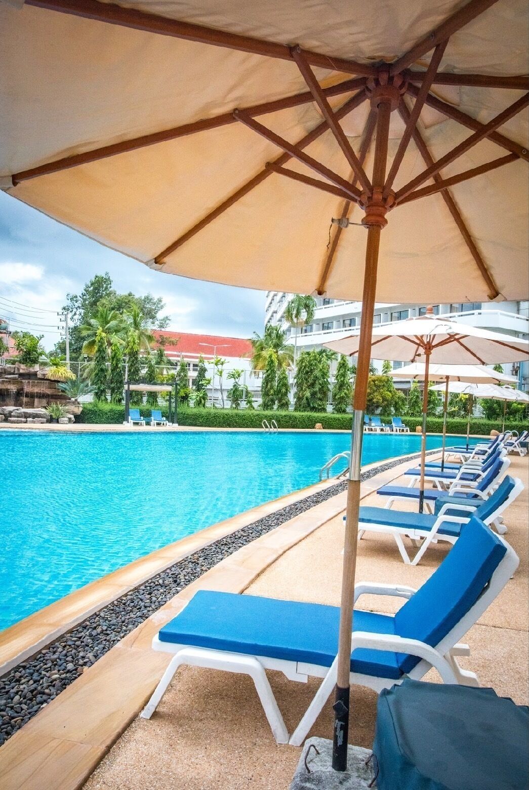 A poolside area with lounge chairs and umbrellas, a clear pool, and a building in the background.