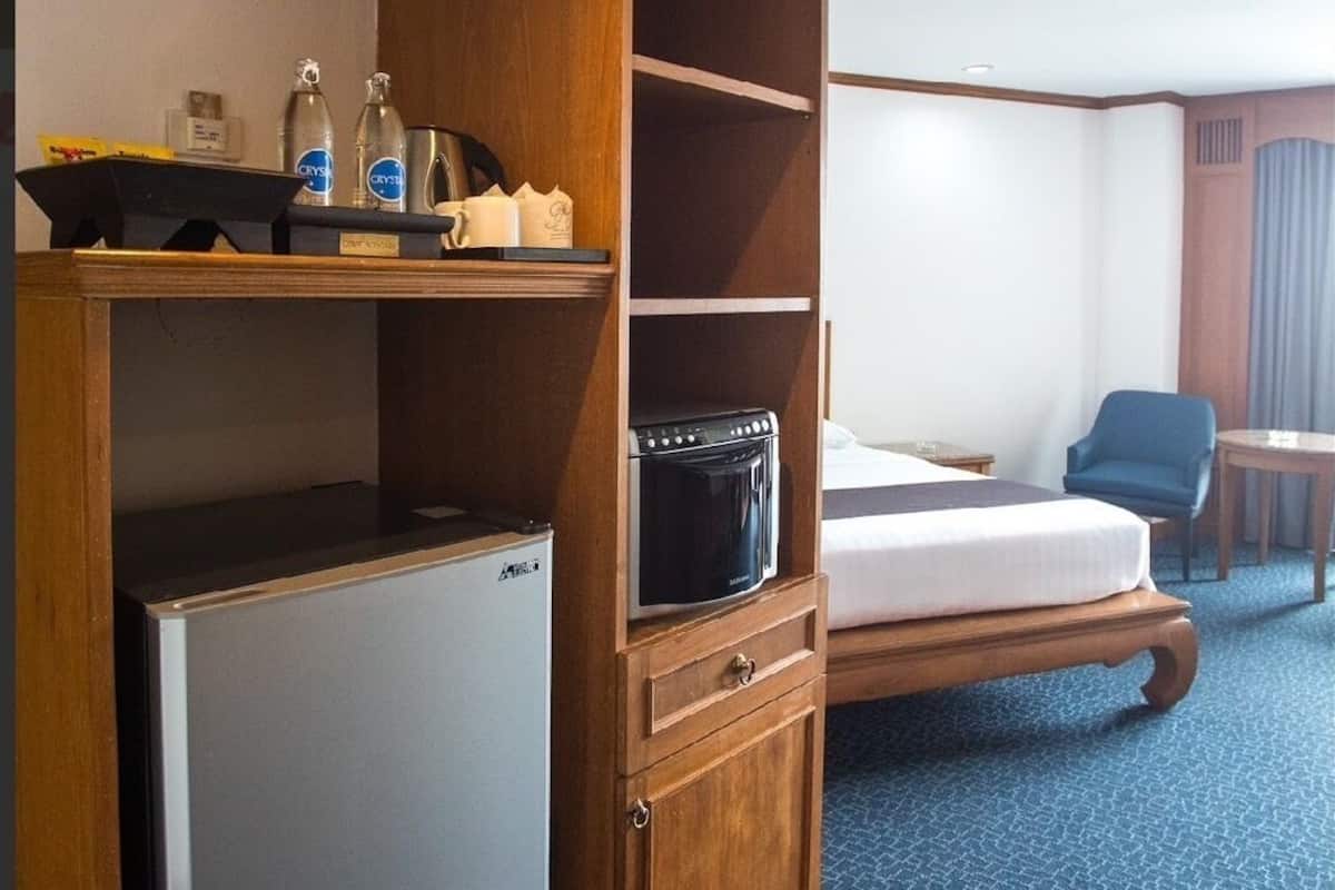 Een compacte hotelkamer met een bed, een klein houten kastje met een magnetron, een koelkast en een plank met toiletartikelen.