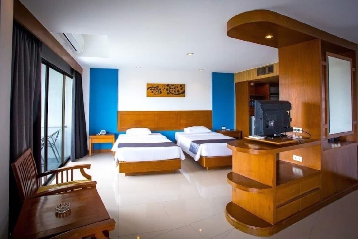 Hotelkamer met twee bedden, een houten bureau, een televisie en een balkon met gordijnen.