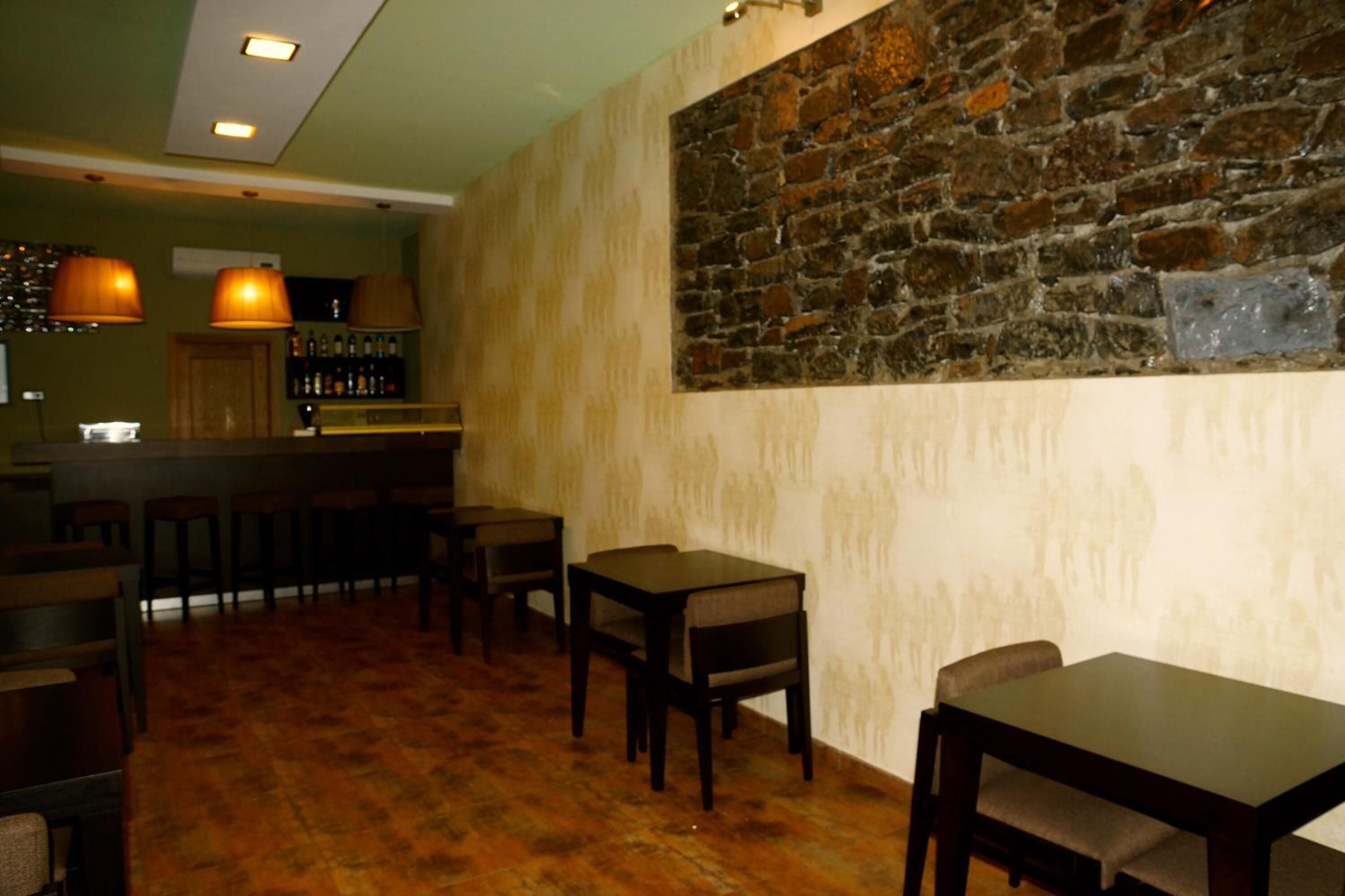 A restaurant with wooden tables and chairs, a stone wall, and hanging pendant lights.