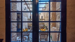 Una vista attraverso una finestra con motivi a griglia, che mostra un edificio in pietra con travi in legno e un balcone.