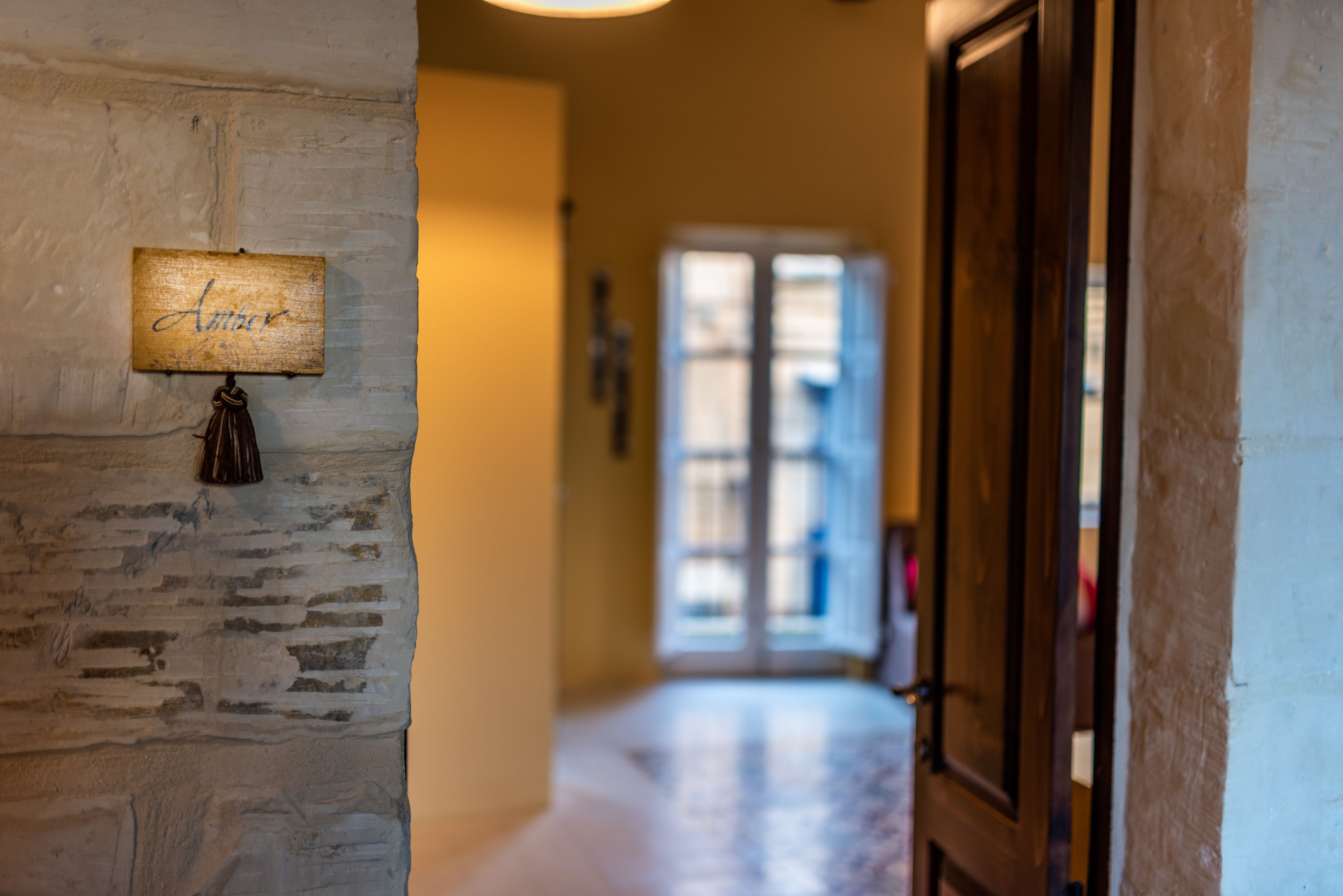 A hallway with a rustic wall, a wooden door, and a window with blinds.