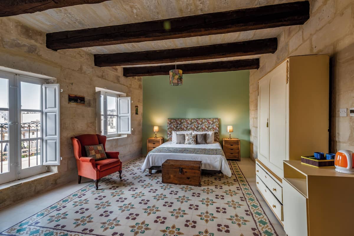 A bedroom with a bed, a chair, a dresser, and a window with a view.