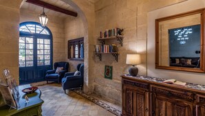 Una stanza con parete in pietra, un mobiletto in legno, una poltrona blu, una libreria e uno specchio grande.