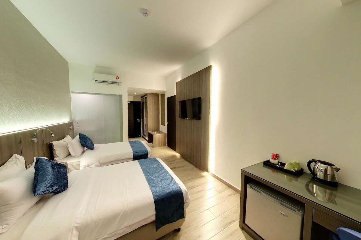 A hotel room with two beds, a desk, a television, and an air conditioning unit.