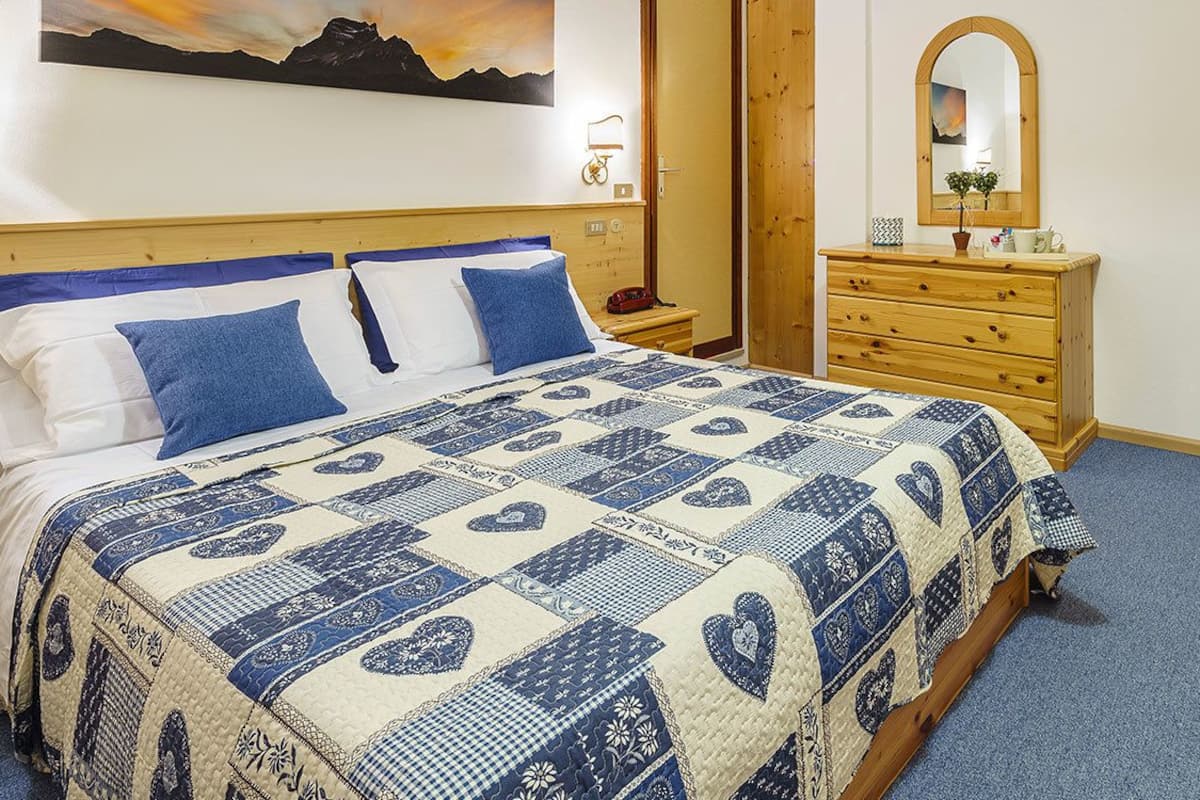 A bedroom with a bed, wooden dresser, and a mirror.